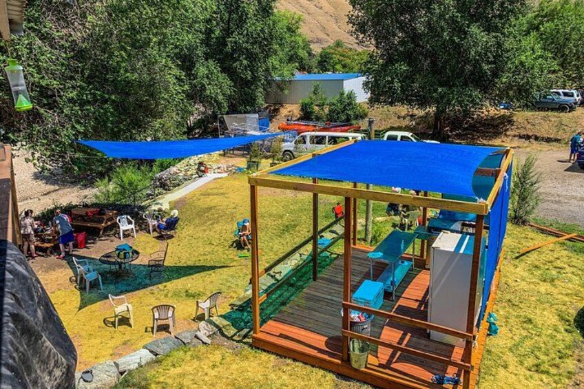 Une terrasse en bois recouverte d’une bâche bleue, entourée d’une pelouse, avec des chaises et des tables. 5