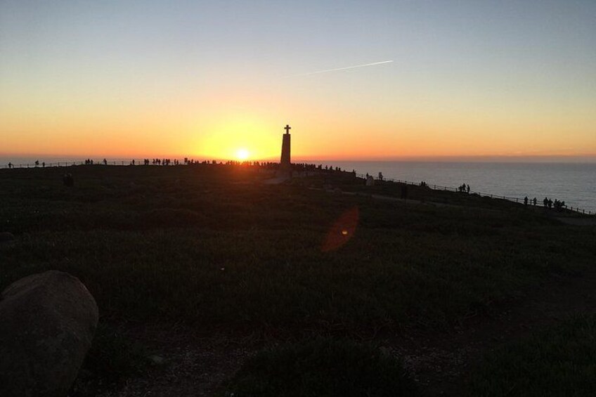 A sunset over a coastal landscape with a lighthouse and people walking along the shore. 3
