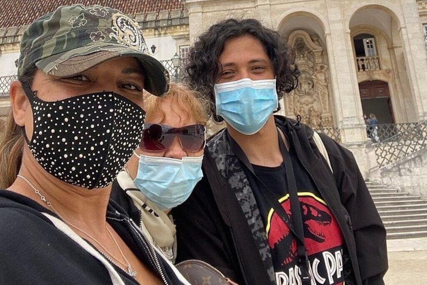 Three people wearing masks, standing in front of a building with classical architecture. 4
