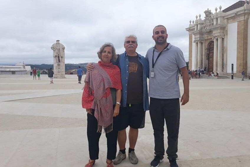 Trois personnes se tiennent sur une place publique, avec un bâtiment historique et une statue en arrière-plan. 3