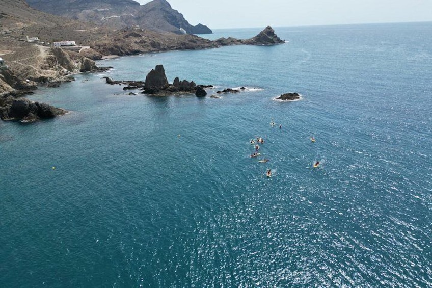 Una zona costera con aguas azules cristalinas, afloramientos rocosos y un grupo de personas haciendo kayak. 2