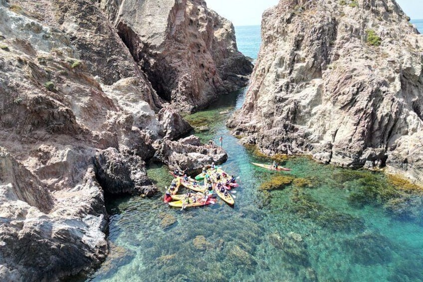 Un grupo de personas haciendo kayak en una zona costera rocosa con agua cristalina. 1