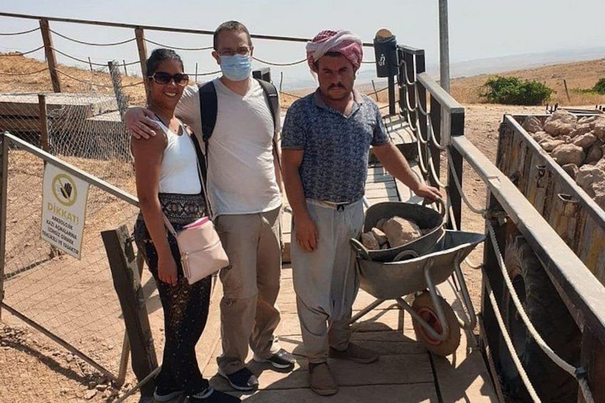 Three people standing on a wooden platform with a wheelbarrow and a fenced area with animals. 1