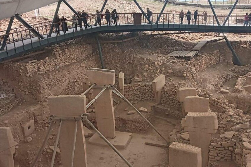 An archaeological site with exposed ruins and a pedestrian bridge. 5