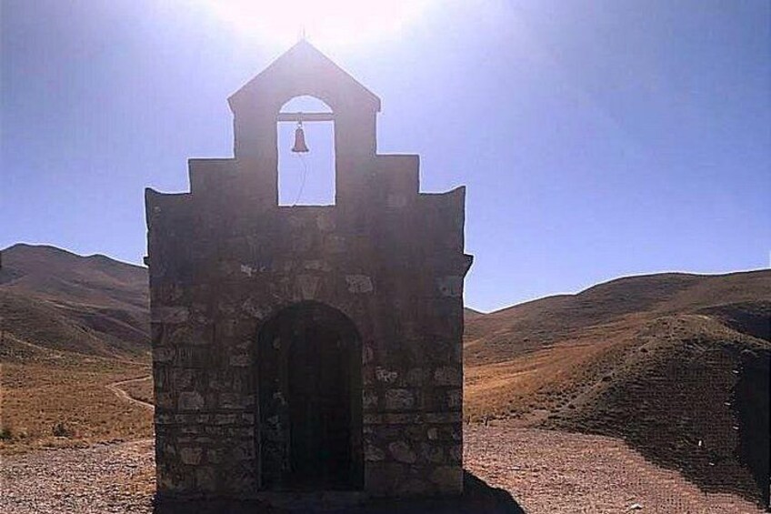 Una torre de campana de piedra con una campana, rodeada por un paisaje árido. 3