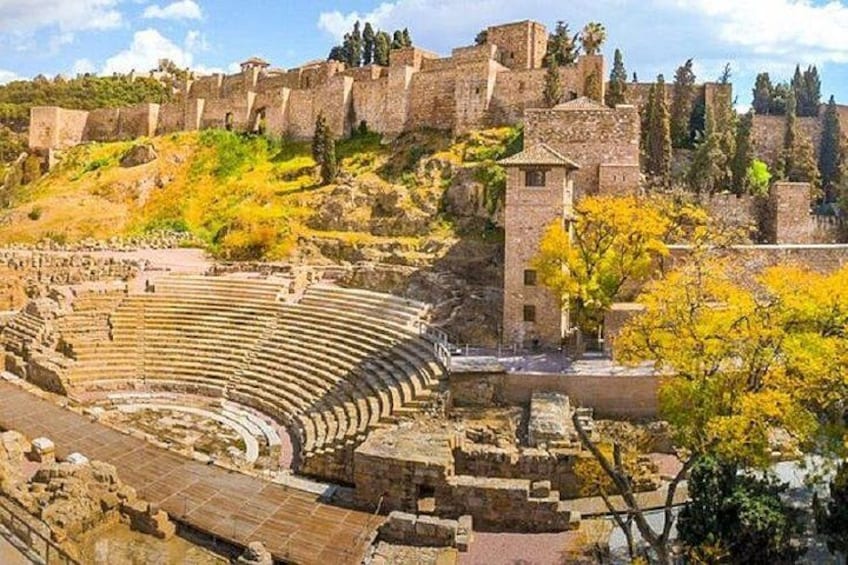 An ancient amphitheater with stone seating, ruins of a wall, and trees with yellow leaves. 1
