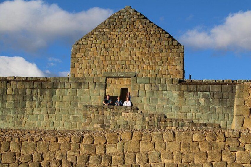 A stone building with a triangular roof, a stone wall, and a clear sky. 5