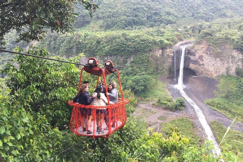 A red cable car with passengers, a waterfall, and lush greenery. 4
