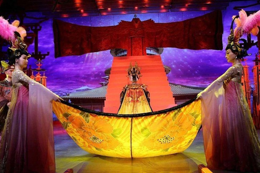 A stage with a central figure in a traditional costume, a large yellow and orange fabric, and a red backdrop with a traditional building. 2