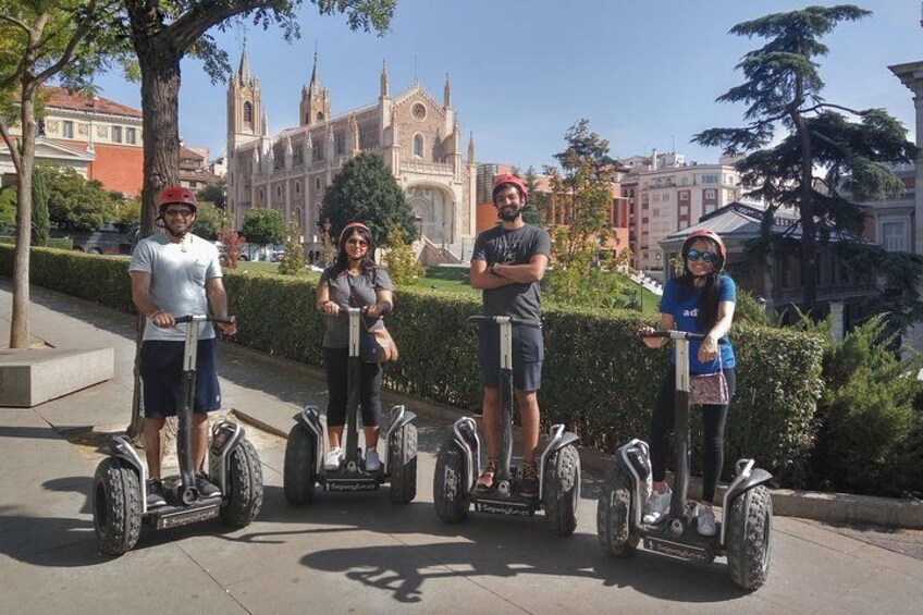 Four people on segways, a large church, and a tree-lined sidewalk. 2