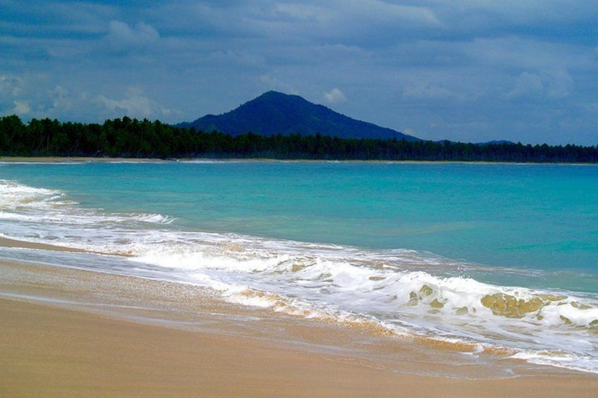 Una playa con agua turquesa, una orilla arenosa y una montaña al fondo. 4
