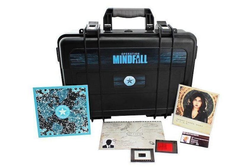 En sort aktetaske mærket 'Operation Mindfall' med en stjerne, et blåt kort med stjernedesign, et fotografi, et kort og en rød genstand. 1