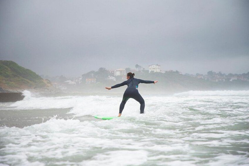 A person surfing on a green board in rough ocean waters with a coastal town in the background. 3