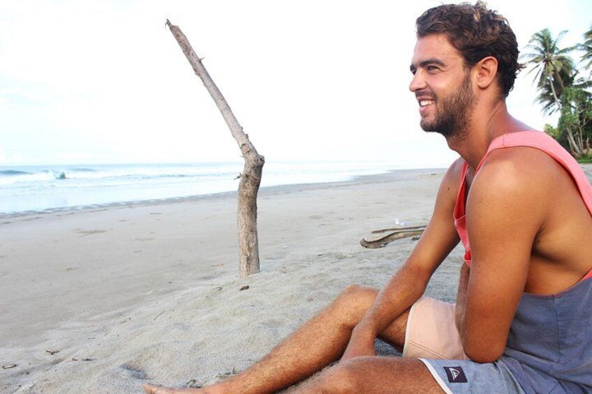 A person sitting on a beach with a tree and ocean in the background. 2