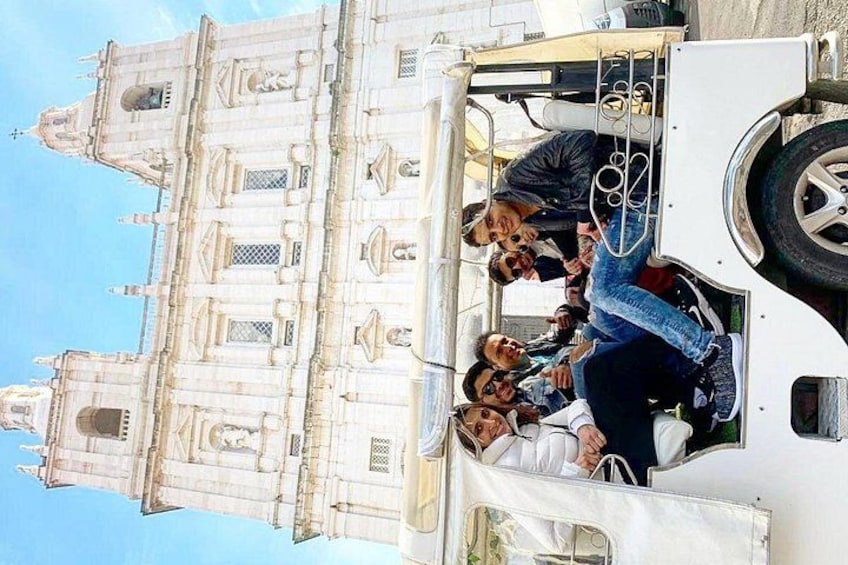 A group of people on a white vehicle near a large, ornate building with multiple towers and spires. 2