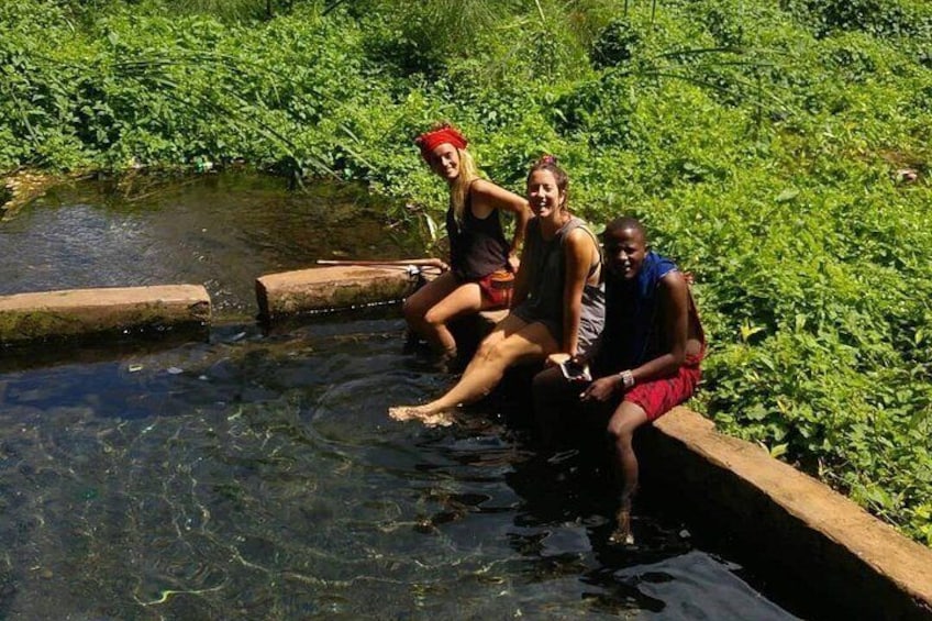 Three people sitting by a clear water body surrounded by greenery. 2