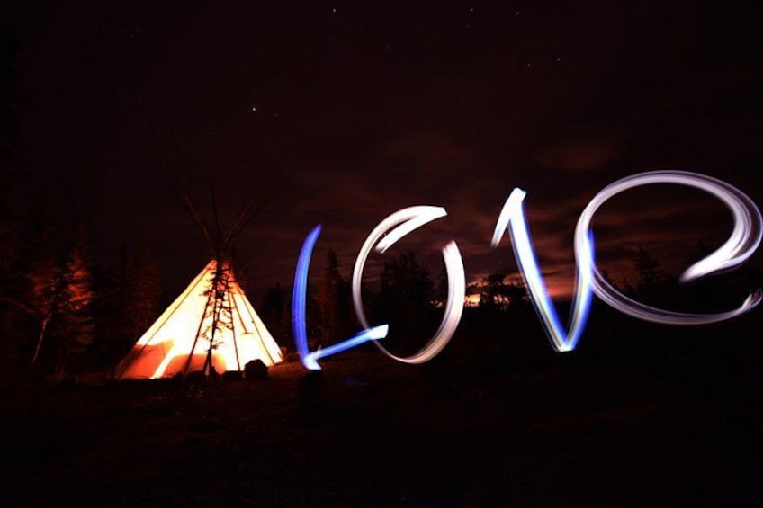 Escena nocturna con una tienda tipi iluminada y la palabra 'LOVE' trazada con luces. 3