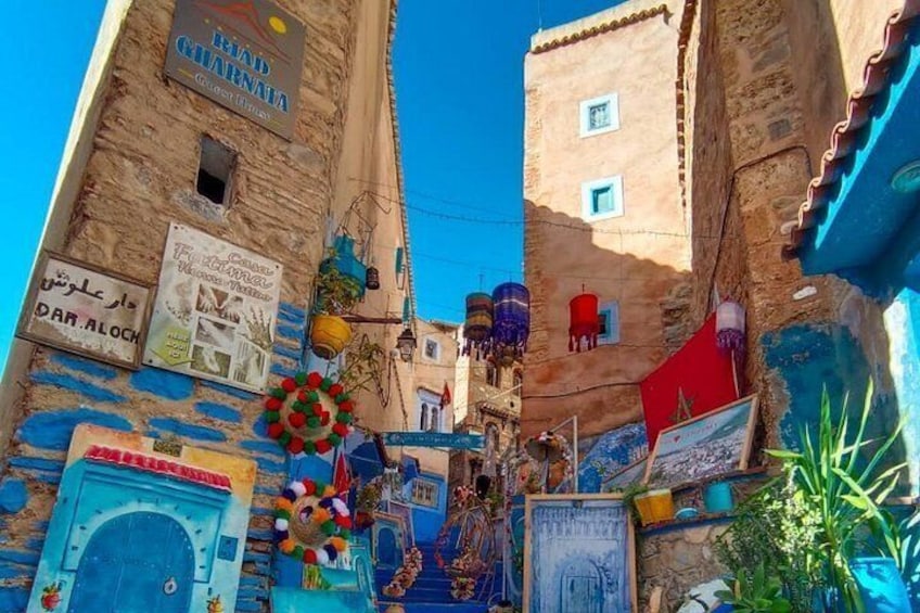 A narrow street with colorful buildings, a blue door, and various signs and decorations. 4