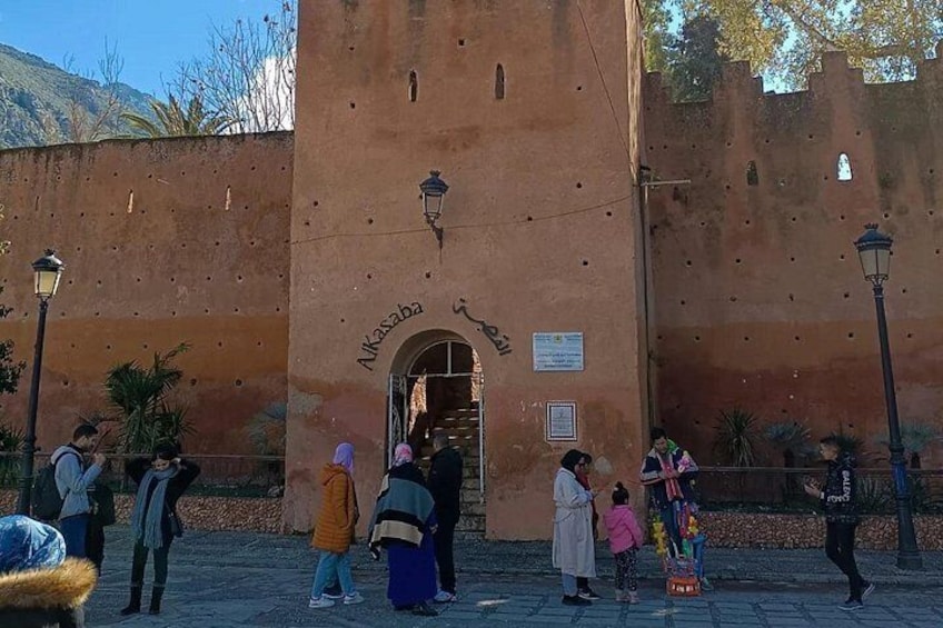 A historic building with an arched entrance labeled 'Alkasaba.' People are gathered around, some taking photos. 2