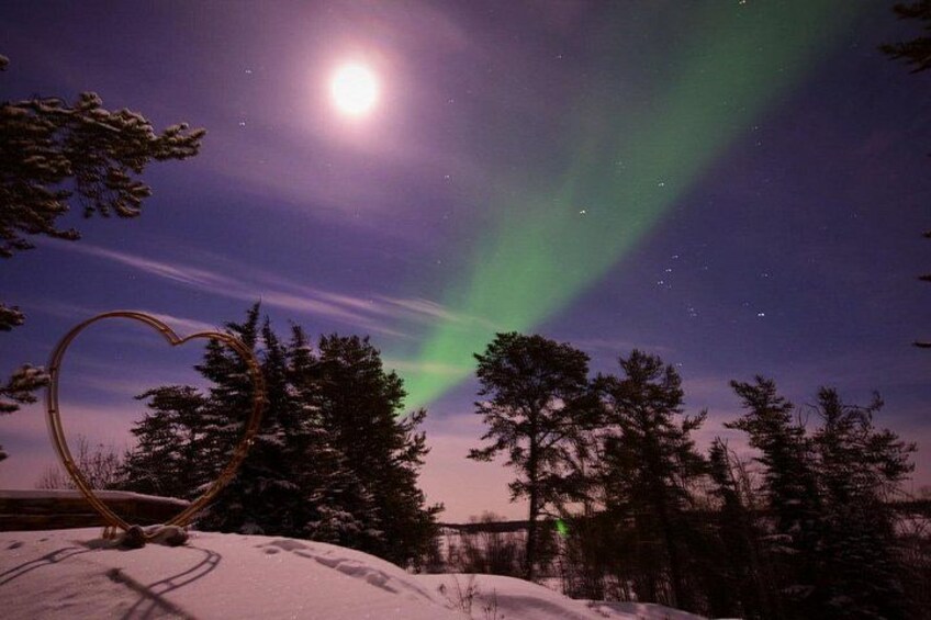 Escena nocturna con luna llena, auroras boreales, suelo cubierto de nieve y una escultura con forma de corazón. 2