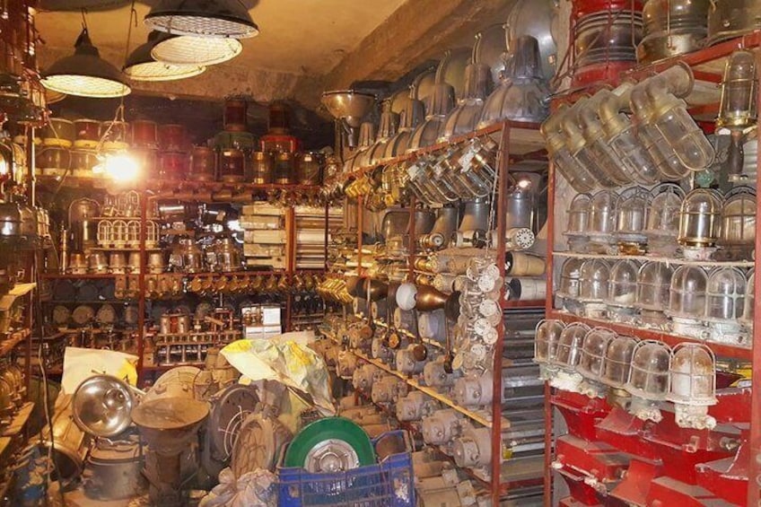 A cluttered shop with shelves filled with various metal objects and containers. 1
