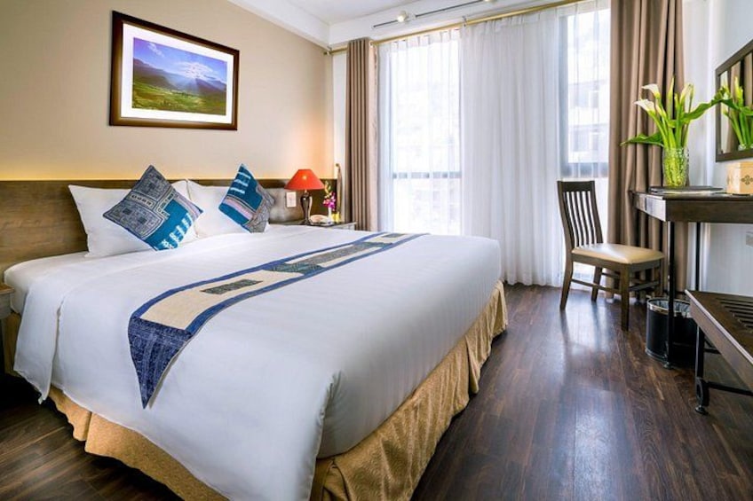 A hotel room with a large bed, a desk, a chair, a lamp, and a picture on the wall. 4