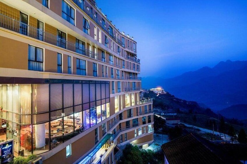 A multi-story hotel with a glass facade, located in a mountainous area with a view of the valley below. 5