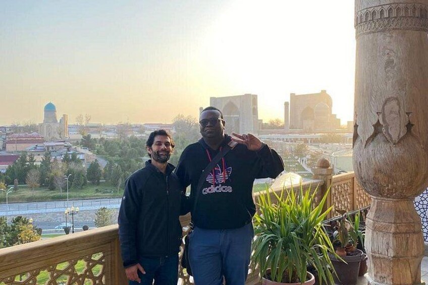 Two people standing on a balcony with a cityscape in the background. 2