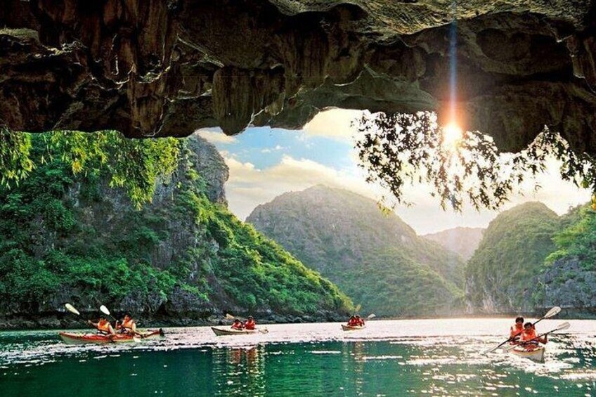 A cave opening with kayaks on a calm river surrounded by lush green hills. 2