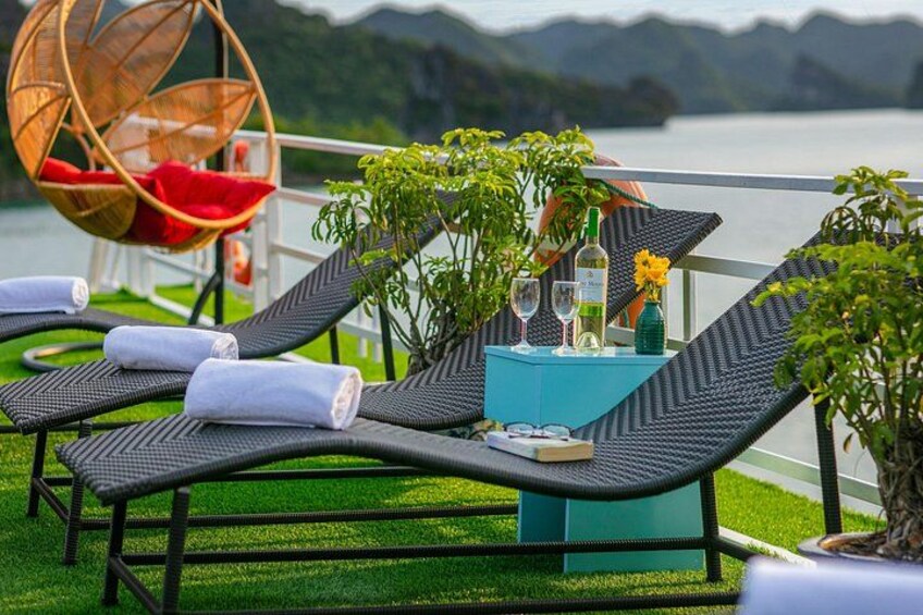 Outdoor lounge chairs, a hanging chair, and a table with drinks and flowers by a lake. 2