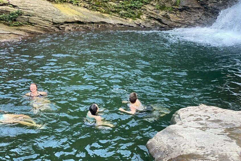 Three people swimming in a natural pool with a waterfall. 4