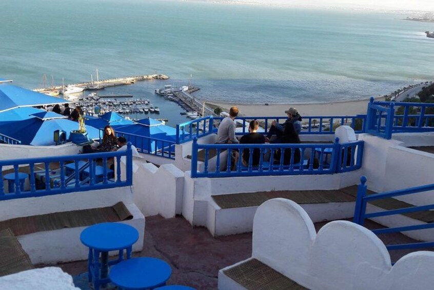 Una terrazza vista mare con ringhiere blu, pareti bianche e una vista sull'oceano e sulle barche. 1