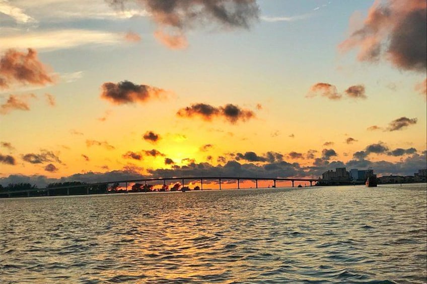 A sunset over a body of water with a bridge and distant city skyline. 4