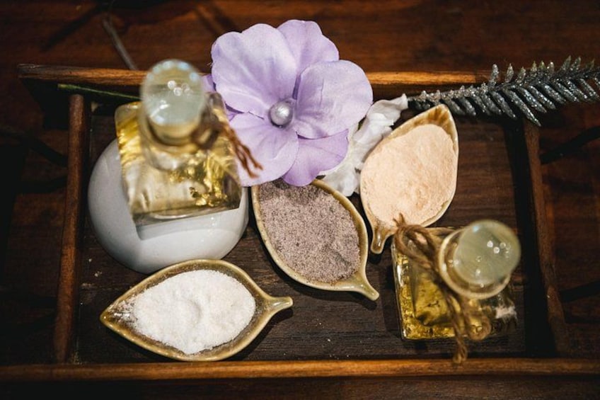 A wooden tray with various spa products including bottles of oil, a flower, and powders. 5
