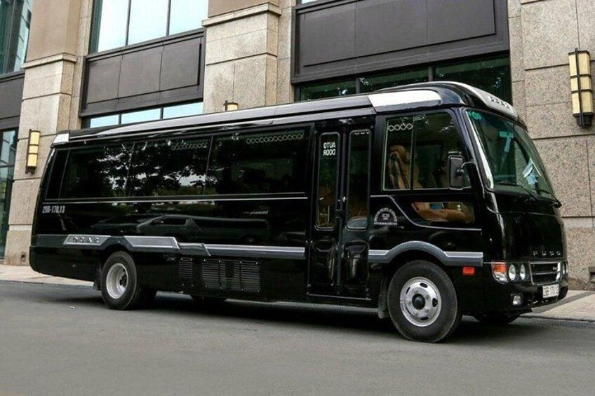 A black bus parked in front of a building with large windows and a stone facade. 2