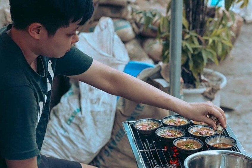 A person cooking food on a grill with several bowls of ingredients and a metal container. 2