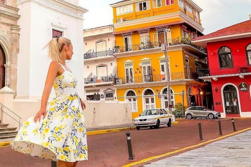 A woman in a floral dress walking on a street with colorful buildings. 5