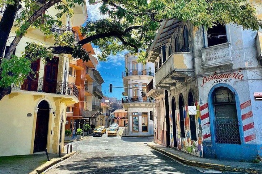A narrow street lined with colorful buildings, a blue storefront, and a clear sky. 4