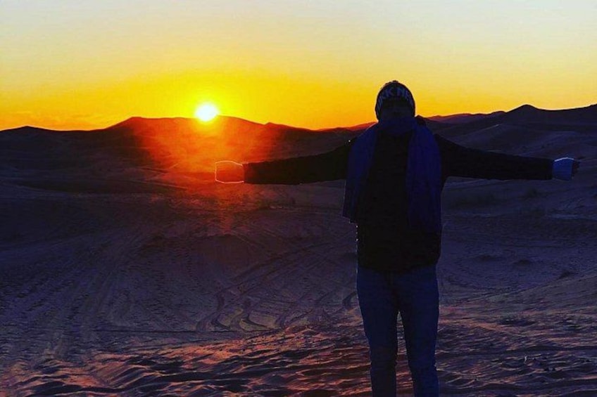 A person standing with arms outstretched in a desert landscape at sunset. 2