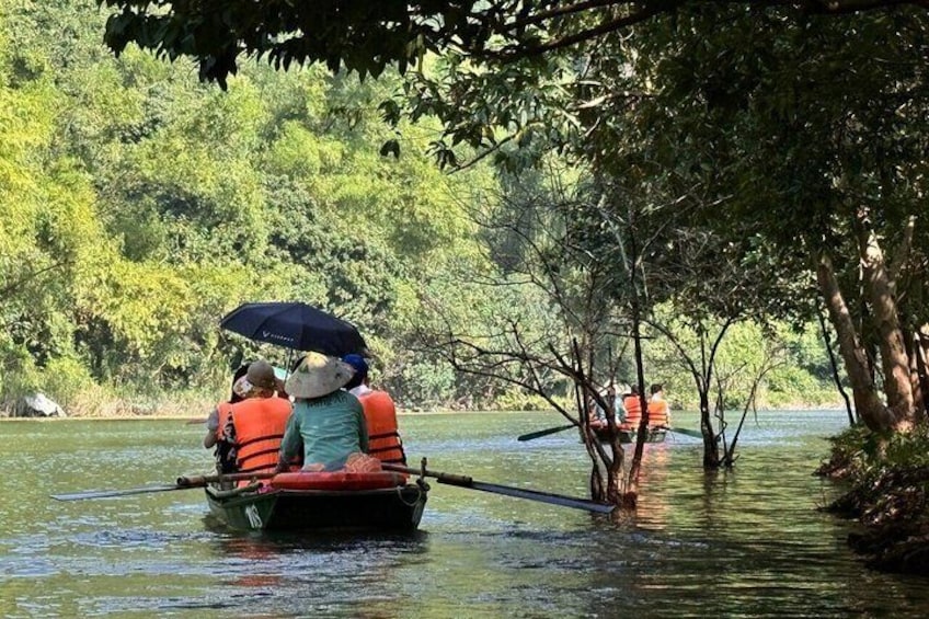 A boat with two people wearing life jackets and an umbrella, surrounded by trees and water. 5