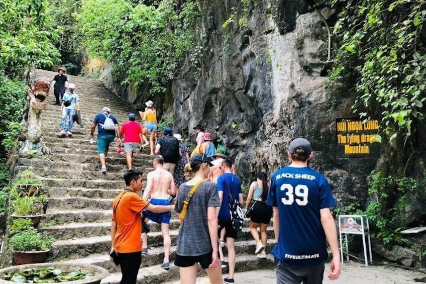 A group of people ascending a stone staircase in a natural setting with greenery and a sign indicating 'NUI HONG LUNG The flying dragon Mountain.' 2