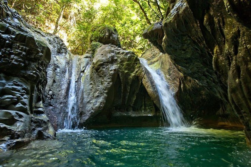 A waterfall cascading into a pool surrounded by rocky terrain and dense foliage. 2