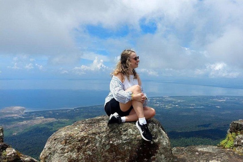 En person sitter på en klippa med en vacker utsikt över en kustlinje och berg i bakgrunden. 1