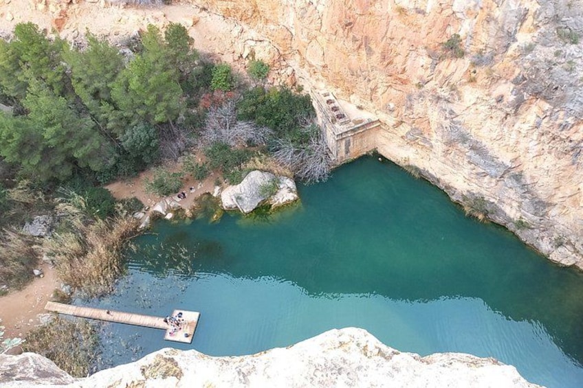A natural pool surrounded by cliffs, a wooden dock, and dense greenery. 5