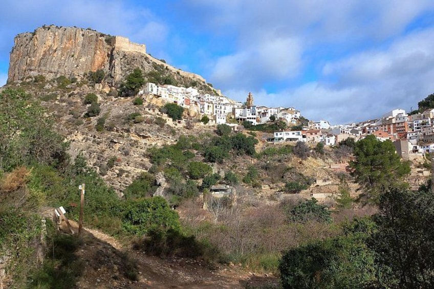 A coastal town with white buildings on a hillside, a rocky cliff, and a clear sky. 2