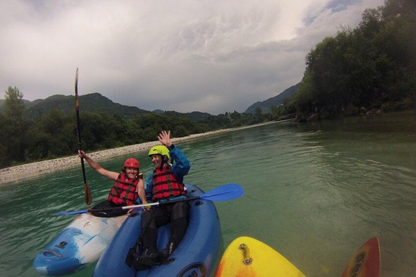 Dos personas kayakendo en un río con una orilla rocosa y colinas verdes al fondo. 4