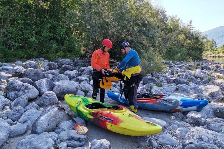 Dos personas preparando kayaks en una orilla rocosa con árboles al fondo. 2