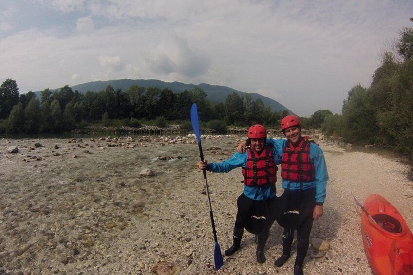 Dos personas con chalecos salvavidas y cascos rojos, una sosteniendo un remo, de pie sobre un sendero de grava con un kayak rojo cerca. 3