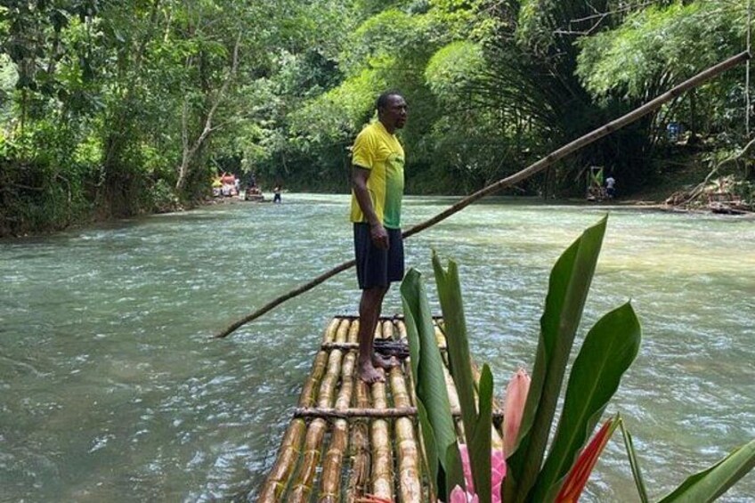 A person standing on a bamboo raft in a river surrounded by dense greenery. 5
