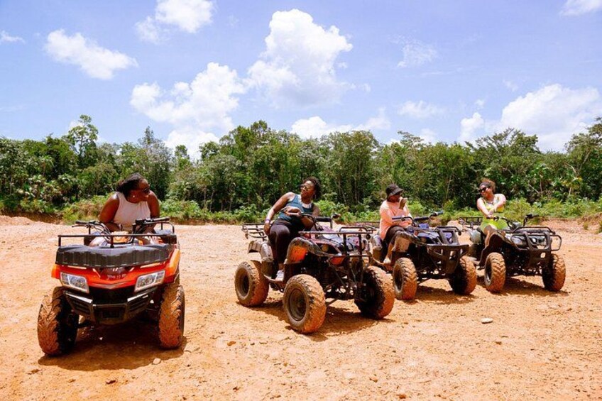 Quatre personnes conduisent des quads sur un chemin de terre, avec des arbres en arrière-plan. 1